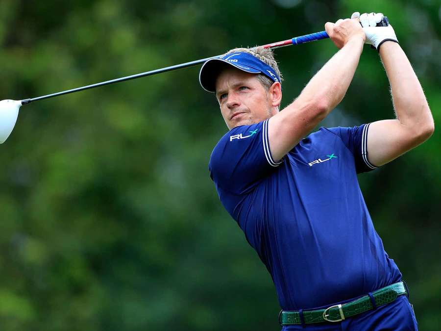 Professional golfer mid-swing on a sunny day with green foliage behind. — Briny Baird Wallpaper