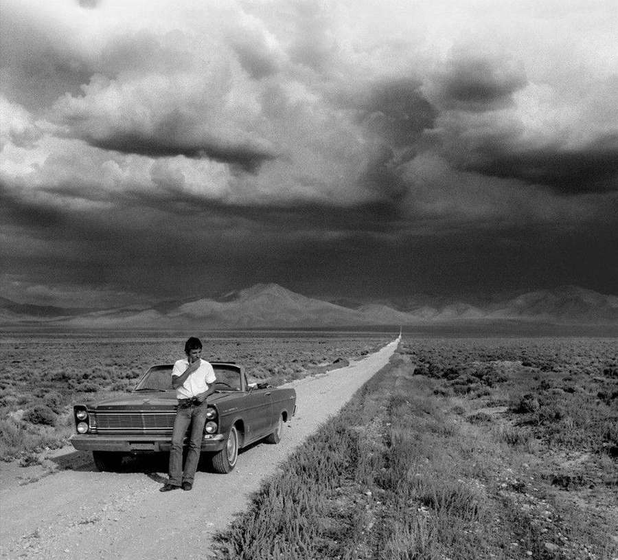 Mann ruht an Oldtimer auf Wüstenstraße unter stürmischem Himmel — Bruce Springsteen Bilder
