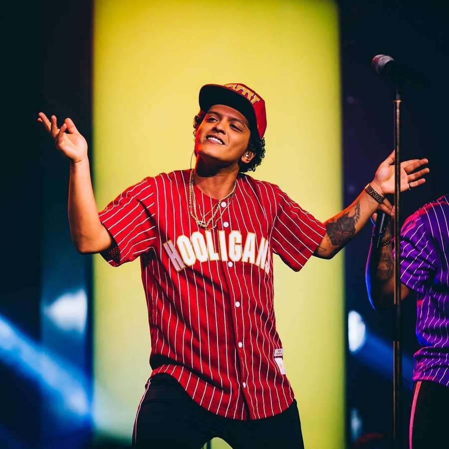 Musician performing on stage in red pinstripe jersey under colorful lights. — Bruno Mars Background