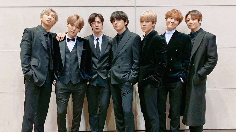 Seven stylish men in black suits posing for a formal group photo against a beige wall. — Bts 2020 Wallpaper
