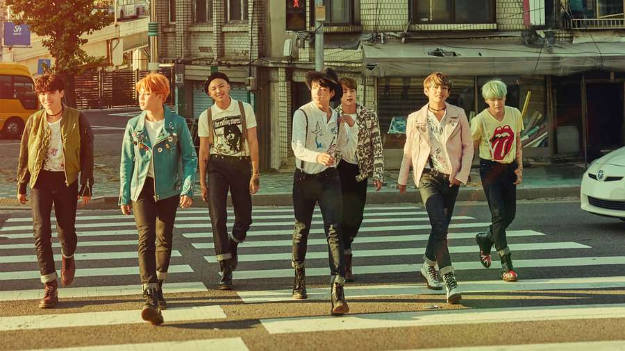 Seven young men with vibrant hair crossing a city street in trendy outfits. — Bts Background