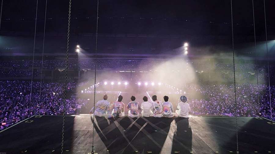 Sechs Künstler sitzen auf einer schwebenden Bühne vor einer riesigen Menge mit lila Lichtern in der Nacht. — Bts Konzert Wallpaper