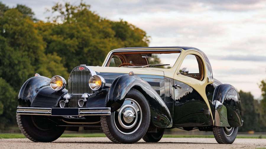 Vintage black and cream Bugatti coupe parked on gravel with trees in background at twilight. — Bugatti Type 41 Royale Wallpaper