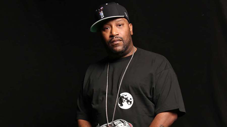 A man wearing a black cap and t-shirt with a moon design looks directly at the camera. — Bun B Wallpaper