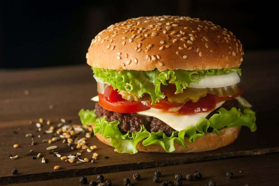 A juicy burger with sesame bun lettuce tomato and cheese on a wooden board with spices. — Burger King Background