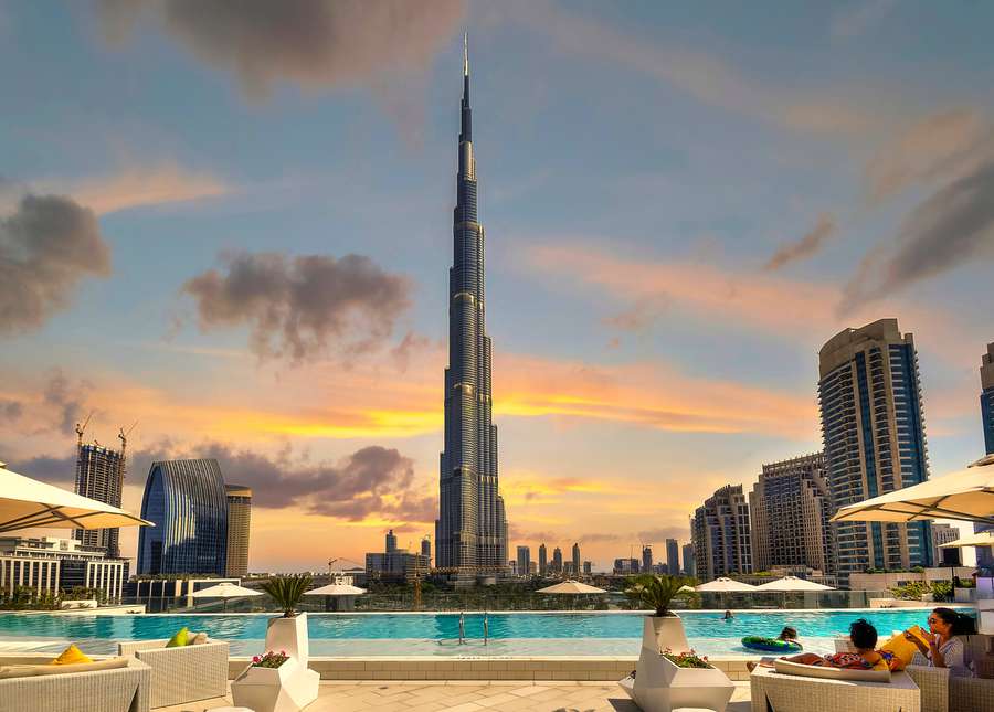 Guests relax by a rooftop pool as the Burj Khalifa stands tall against a sunset sky. — Burj Khalifa Background