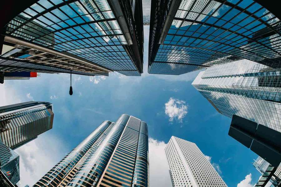 Low-angle view of modern glass skyscrapers reaching toward a blue sky with clouds. — Business Background