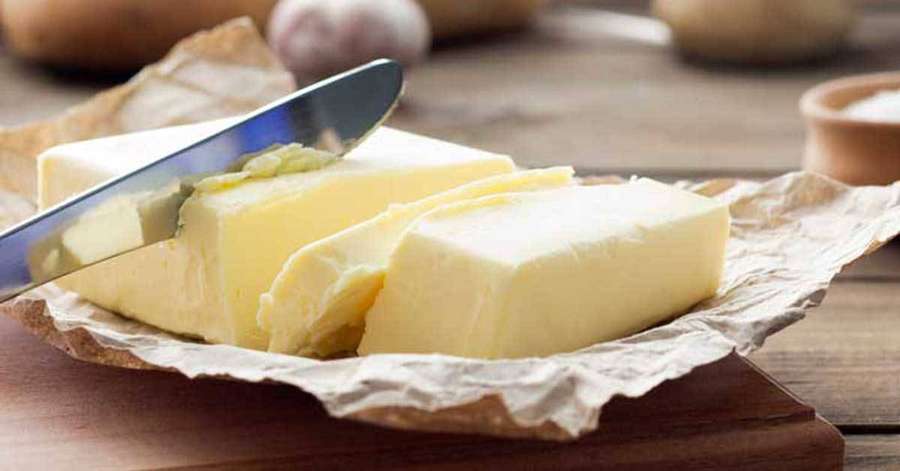 Geschnittene Butter auf Backpapier mit einem Messer auf einem Holzbrett. — Butter Wallpaper