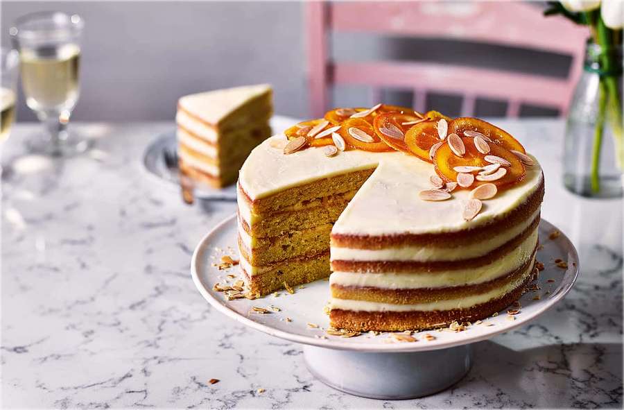 A sliced layered orange cake with almond garnish on a marble countertop. — Buttercream Wallpaper