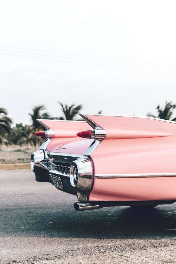 Pink vintage Cadillac with chrome tailfins parked near palm trees at sunset. — Cadillac iPhone Picture