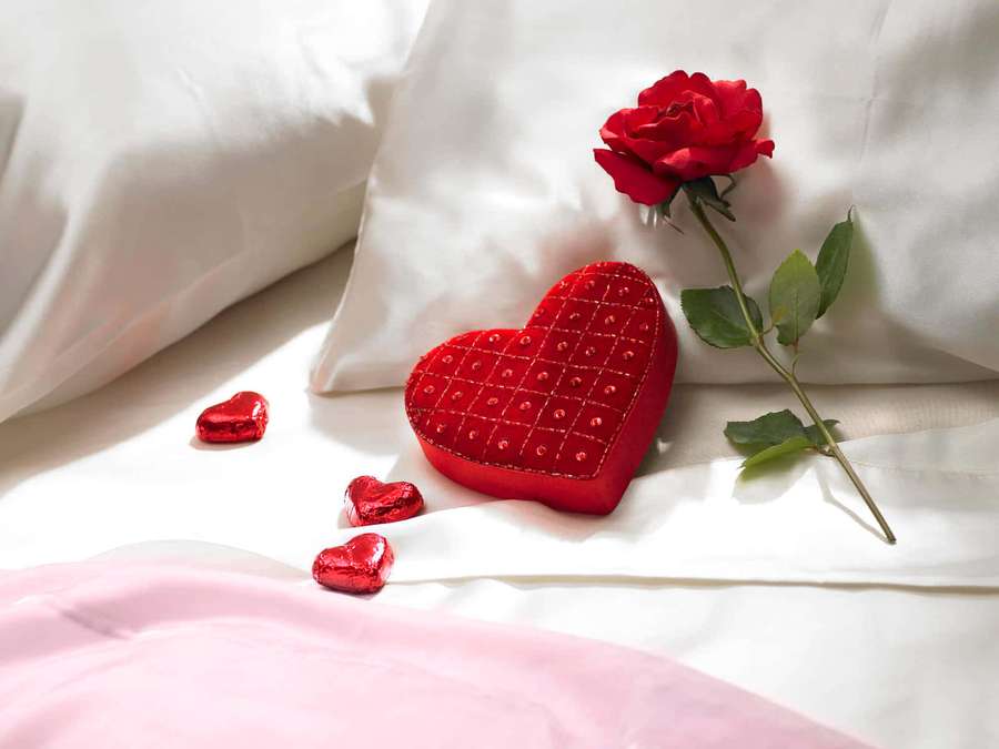 Rosa roja y chocolates corazón en una cama con almohadas blancas y manta rosa. — Caja de Chocolate Fondos de pantalla