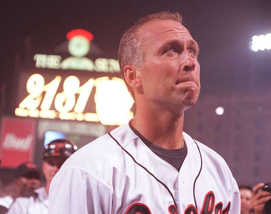 Baseballspieler in weißer Uniform, der nachts zu den Stadionlichtern aufblickt. — Cal Hintergrundbild