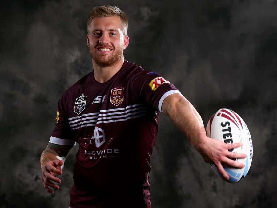 Rugby player in maroon jersey holding a rugby ball with a confident smile. — Cameron Munster Wallpaper
