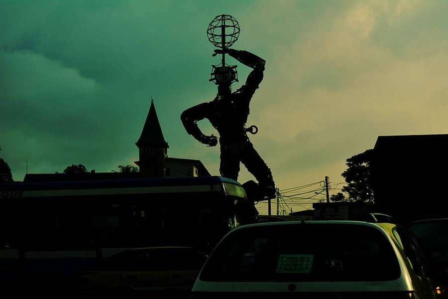 Estatua silueteada sosteniendo un globo sobre una concurrida calle de la ciudad al atardecer. — Camerún Fondos de pantalla