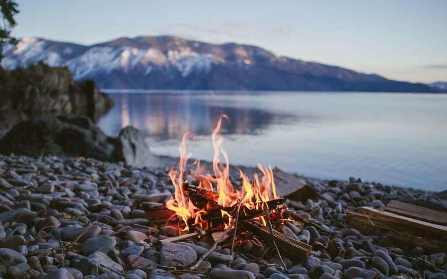 Campfire on rocky shore with snowy mountains and lake at dusk — Campfire Background
