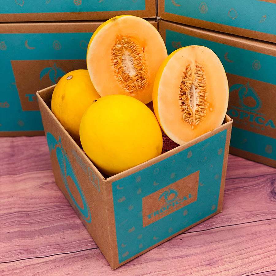 Sekotak melon kuning segar, beberapa dipotong, di atas meja kayu merah muda. — Canary Melon Wallpaper