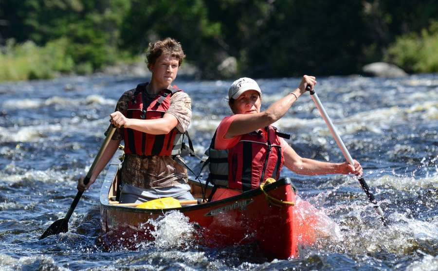 Dos personas remando una canoa roja a través de rápidos de aguas bravas en un río boscoso. — Canotaje Fondos de pantalla