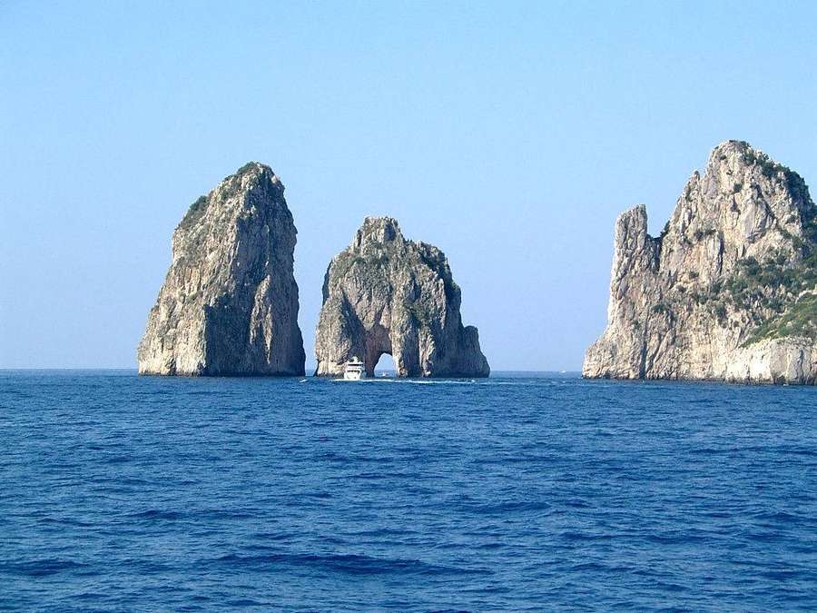 Barco pasando por el arco de las rocas Faraglioni de Capri en el mar azul. — Capri Italia Fondos de pantalla