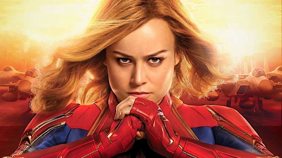 Captain Marvel in red and blue suit with fighter jets in background at sunset. — Captain Marvel HD Wallpaper