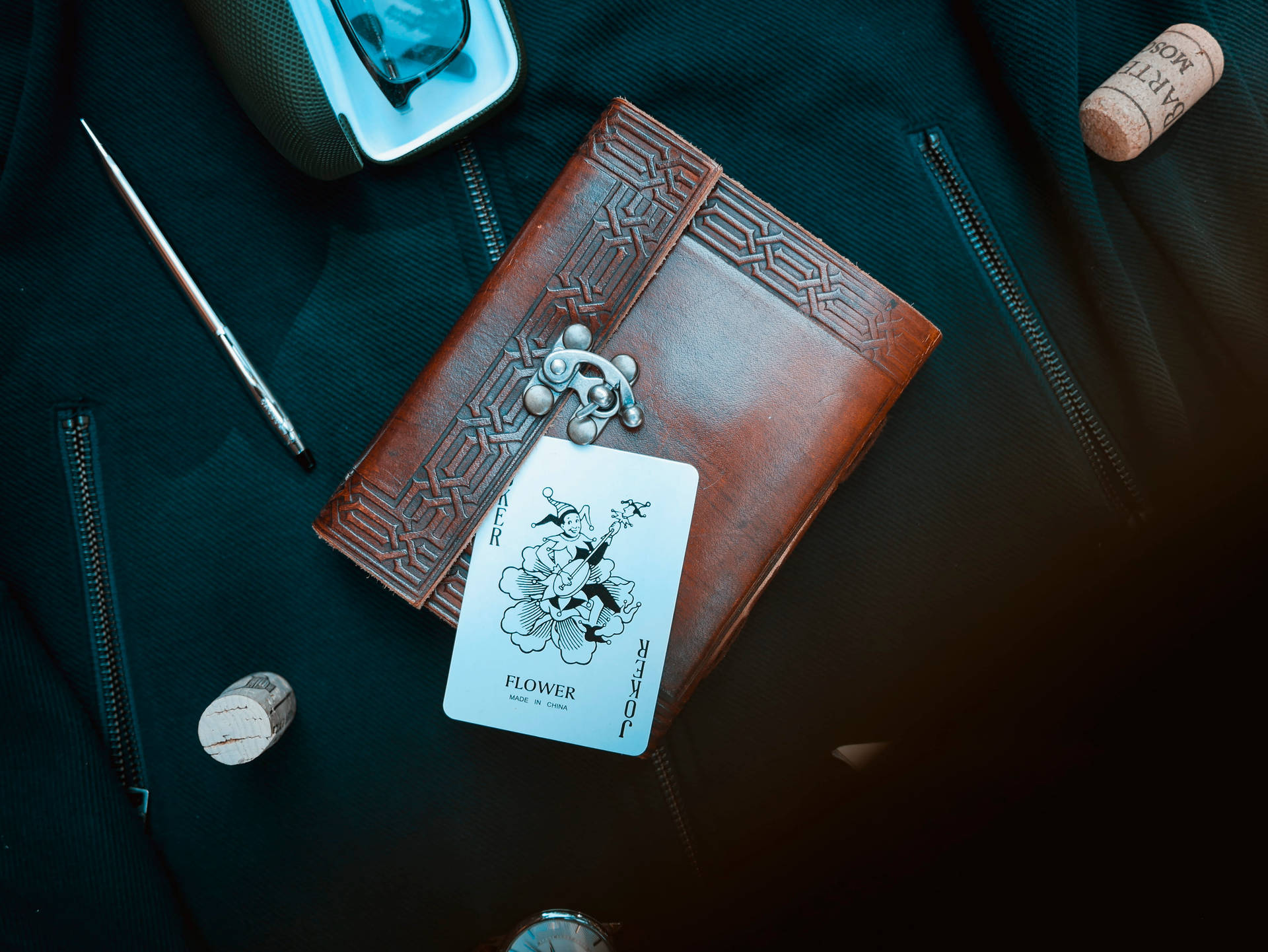 Un diario in pelle con una carta joker e una penna su una superficie scura e strutturata. — Carte Sfondi