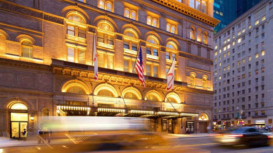 Grand hotel illuminated at dusk with blurred cars passing by on city street. — Carnegie Hall Background