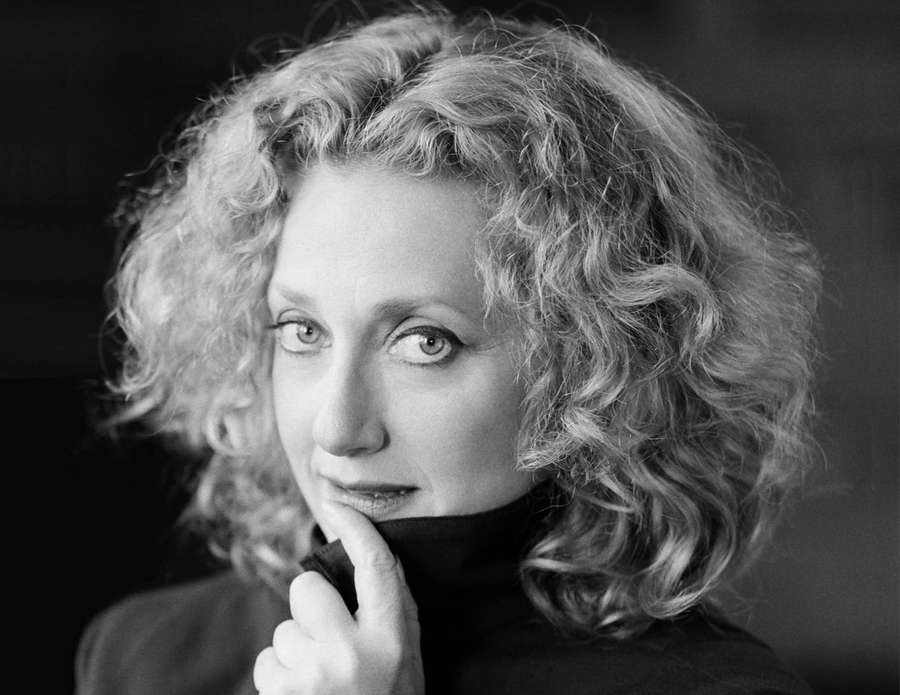 A woman with curly hair looks thoughtfully at the camera with her hand under her chin. — Carol Kane Wallpaper