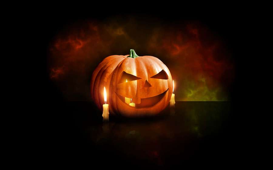 A carved pumpkin with a scary face lit by candles in a dark smoky setting. — Carved Pumpkin Wallpaper