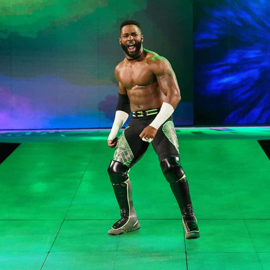 Lutador com equipamento preto e verde rugindo em um palco verde com iluminação colorida. — Cedric Alexander Papéis de Parede