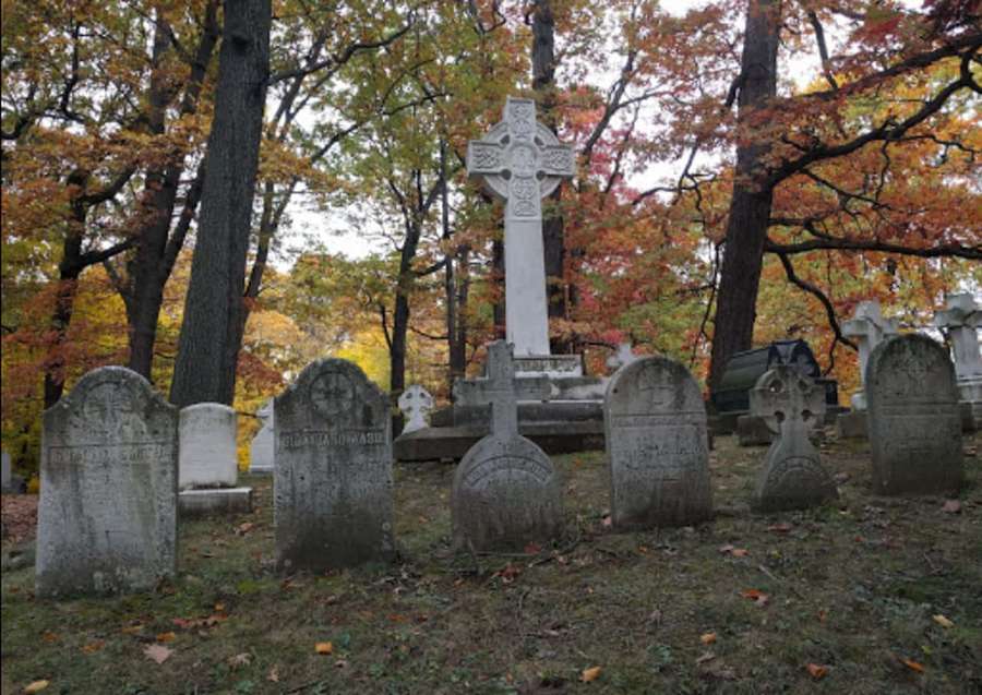 Gravestones and a Celtic cross in a quiet autumn cemetery with colorful foliage. — Cemetery Background