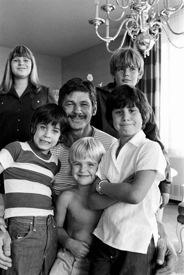Ein lächelnder Mann mit fünf Kindern, die zusammen in einem Zuhause posieren. — Charles bronson Bilder