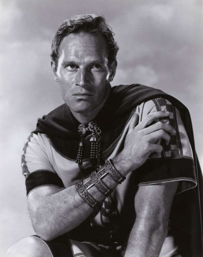 Un hombre de aspecto serio con traje romano, brazaletes detallados y una capa drapeada. — Charlton Heston Fondos de pantalla
