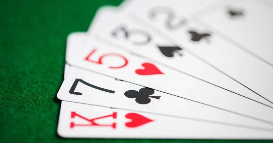 Five playing cards fanned on green felt showing king seven five and two of hearts and spades. — Cheat Background