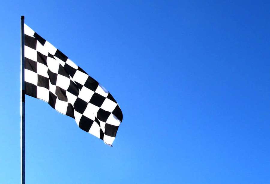 Black and white checkered racing flag waving in the wind against a clear blue sky. — Chequered Flag Wallpaper