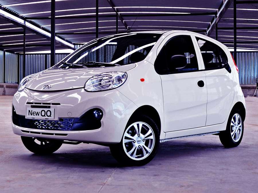 White compact car displayed in industrial warehouse with metal beams and concrete floor. — Chery Qq Wallpaper