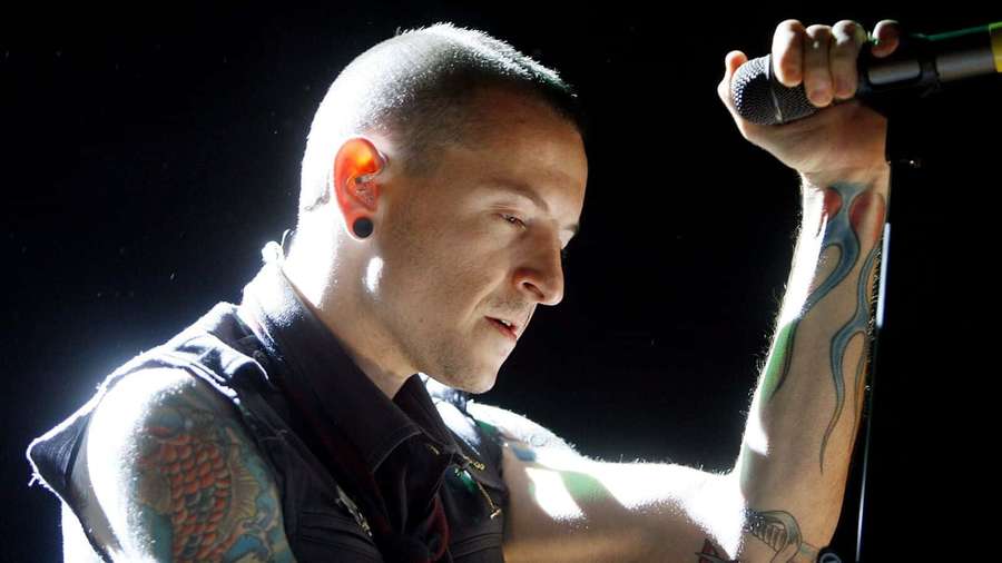 Tattooed male singer performing on stage with microphone under bright lights. — Chester bennington Wallpaper