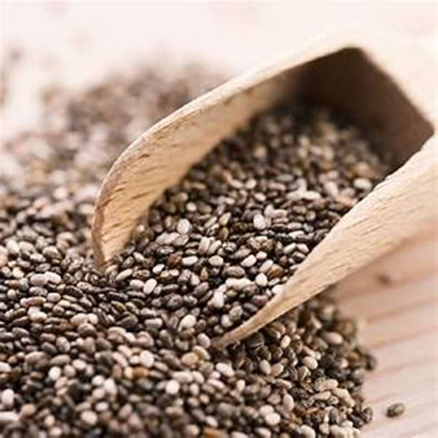 Wooden scoop pouring chia seeds onto a wooden surface. — Chia Seeds Wallpaper