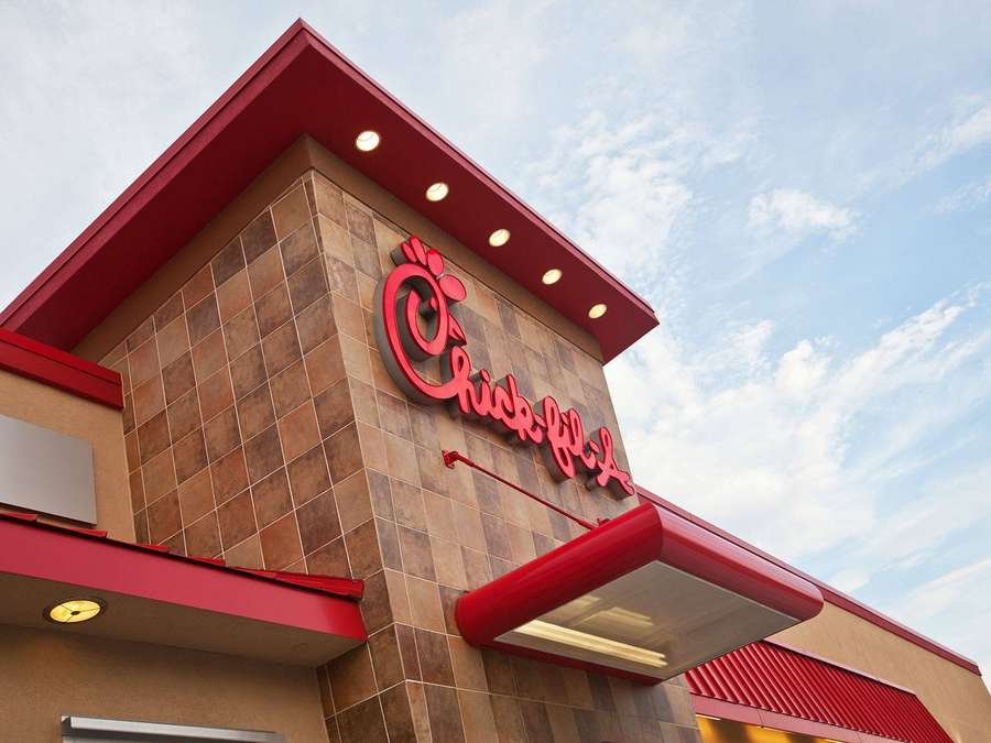 Chick-fil-A restaurant exterior with red accents and tiled walls under a blue sky. — Chick Background
