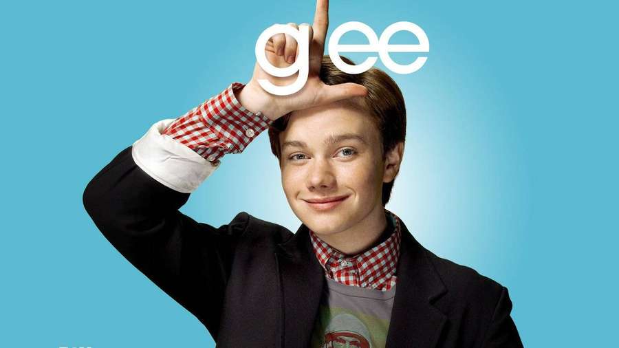Giovane sorridente che forma la parola 'glee' con la mano su sfondo blu. — Chris colfer Sfondi