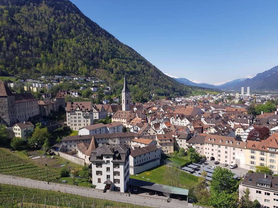 A picturesque town with red roofs and a church tower surrounded by mountains and vineyards. — Chur Wallpaper