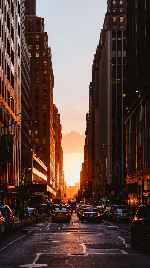 Pôr do sol entre altos edifícios da cidade com carros em uma rua movimentada. — Cidade, pôr do sol, iPhone Papéis de Parede