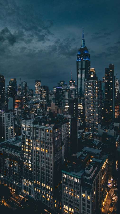 Horizonte de la ciudad de Nueva York al atardecer con edificios iluminados y nubes oscuras. — Cielo Oscuro Fondos de pantalla