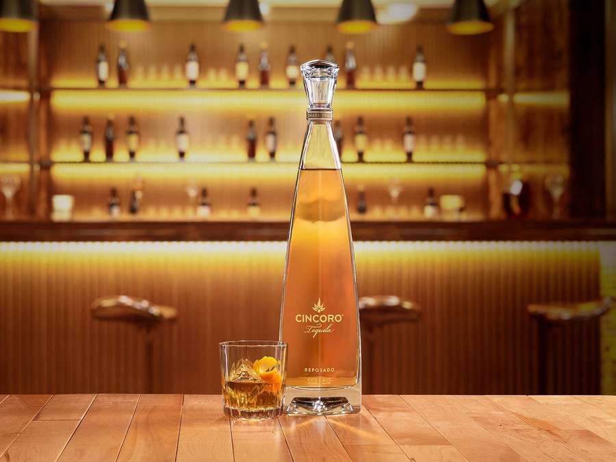 Garrafa de tequila Cincoro Reposado e copo com gelo e guarnição de laranja em um bar de madeira. — Cincoro Papéis de Parede