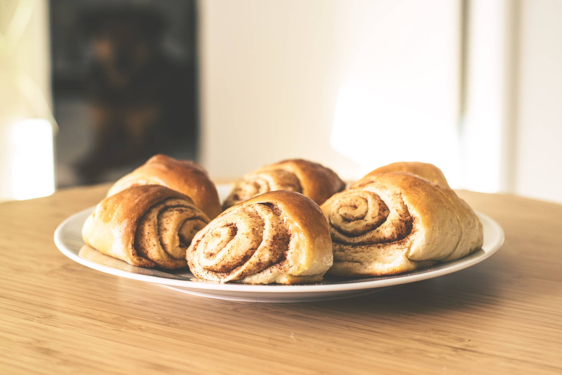 Nybakade kanelbullar på en vit tallrik på ett träbord. — Kanel bakgrund Bakgrundsbilder