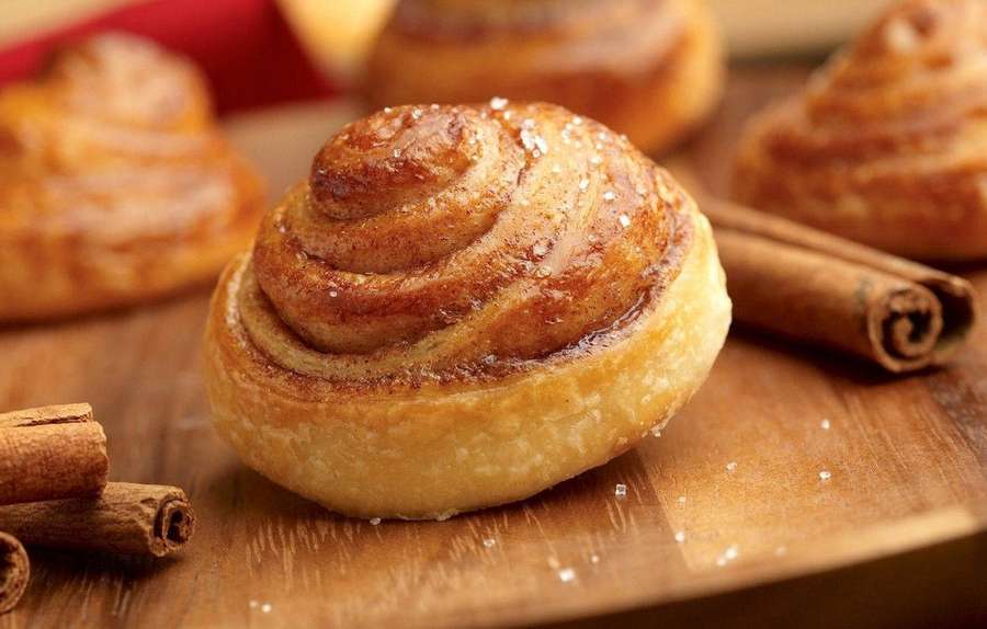 Freshly baked cinnamon roll with sugar on wooden board with cinnamon sticks. — Cinnamon Background