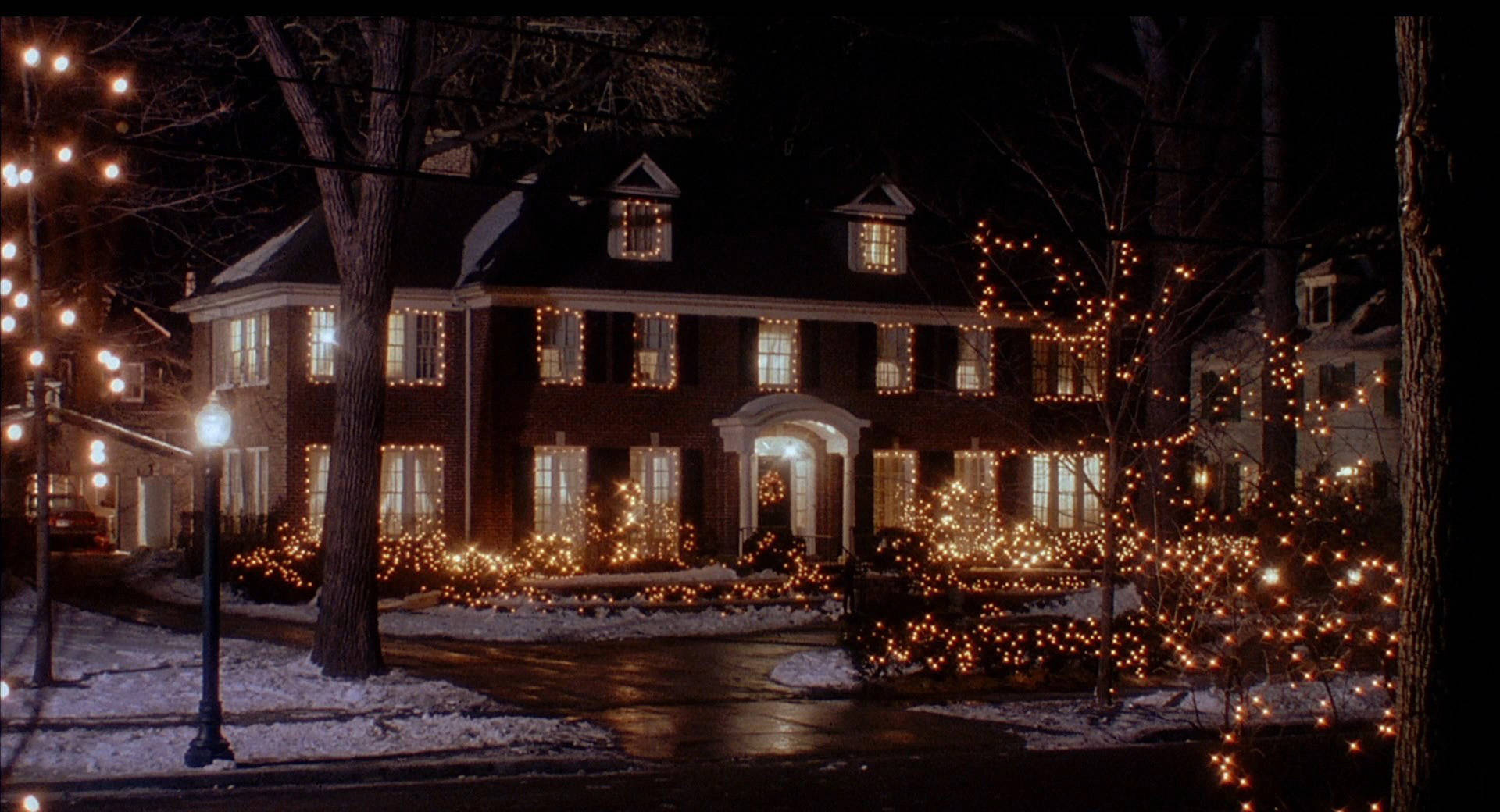 Uma casa coberta de neve decorada com cordões de luzes brilhantes à noite. — Clássico Papéis de Parede