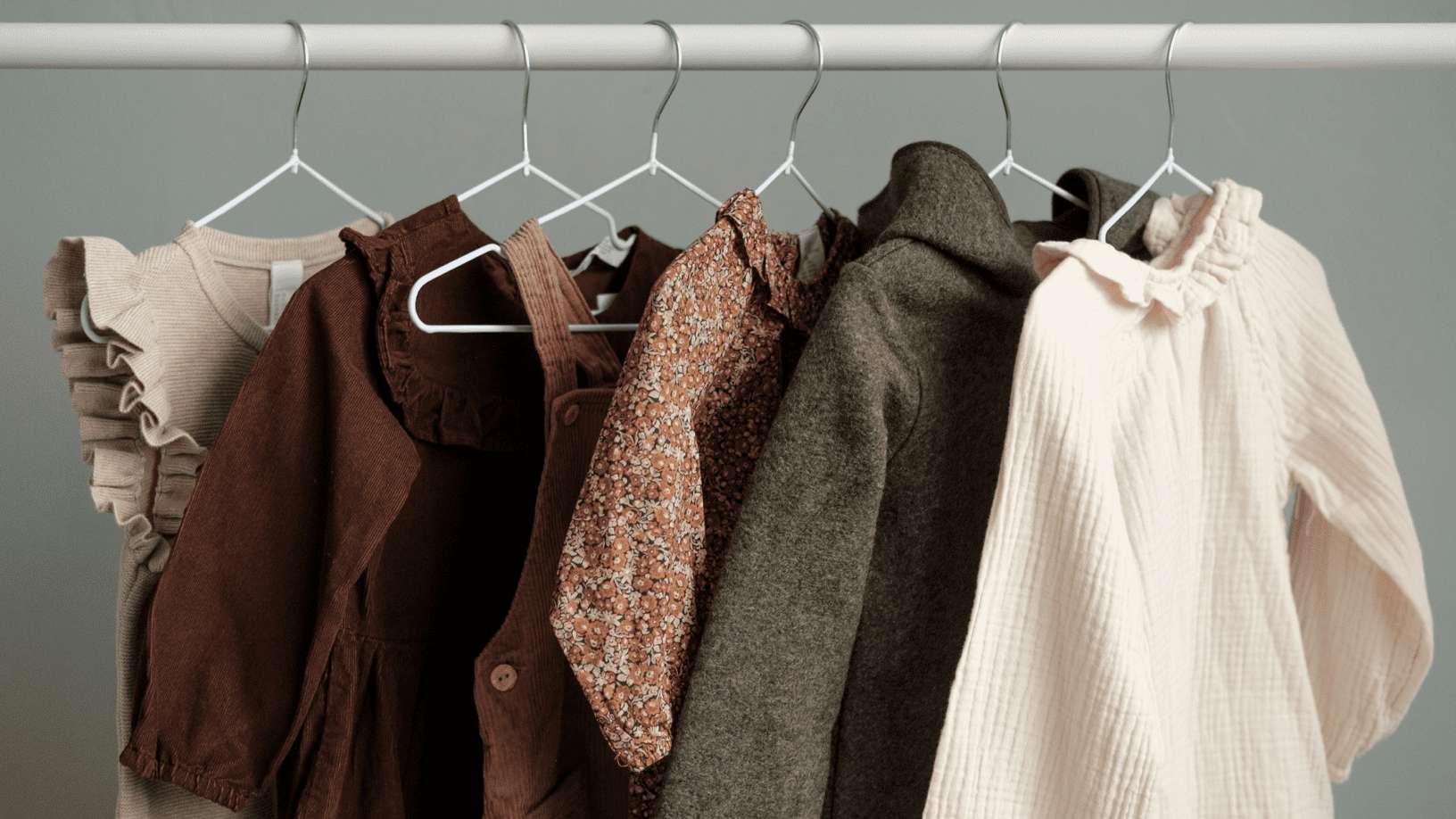 Neatly arranged women's clothing on white hangers against a gray wall. — Clothes Background