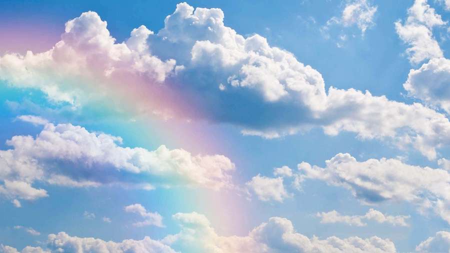 A colorful rainbow arches over soft white clouds in a clear blue sky. — Cloudy Background