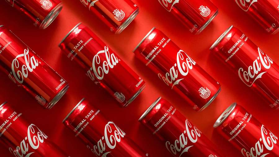 Red Coca-Cola cans arranged diagonally on a matching red surface. — Coca cola Background