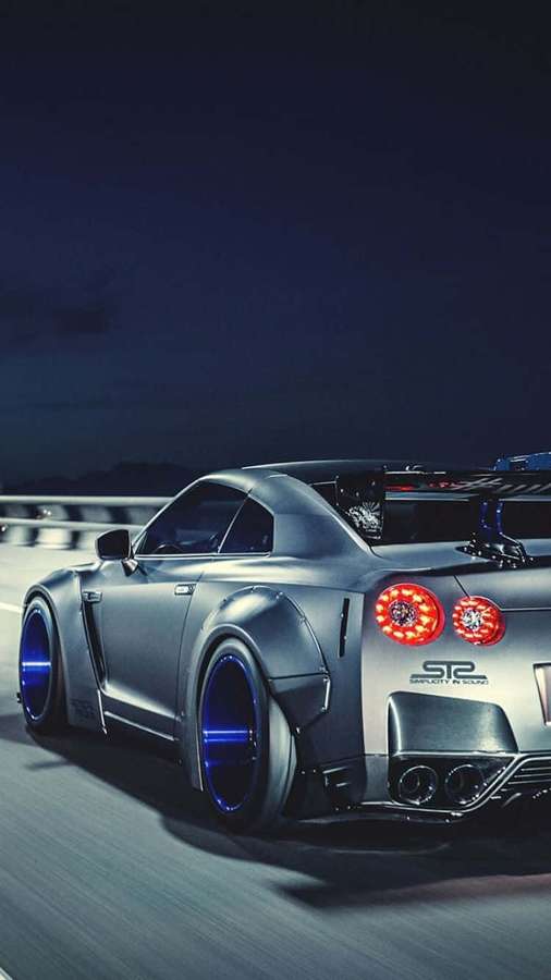 Nissan GT-R ST2 plateado acelerando de noche con luces traseras rojas brillantes y llantas azules. — Coches iPhone Fondos de pantalla