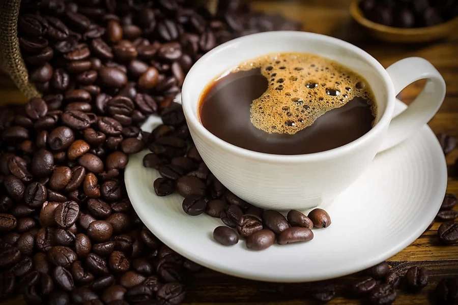 A white coffee cup with foam surrounded by roasted coffee beans on wood. — Coffee Picture